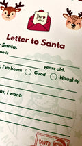 A close-up of a Christmas-themed 'Letter to Santa' writing sheet. The white paper features red and green text, illustrated reindeer heads, a red envelope with a 'Dear Santa' card, and faint green Santa illustrations in the background.